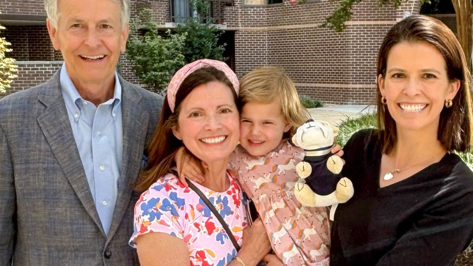 two women, a toddler and a man in a gray suit stand with each other