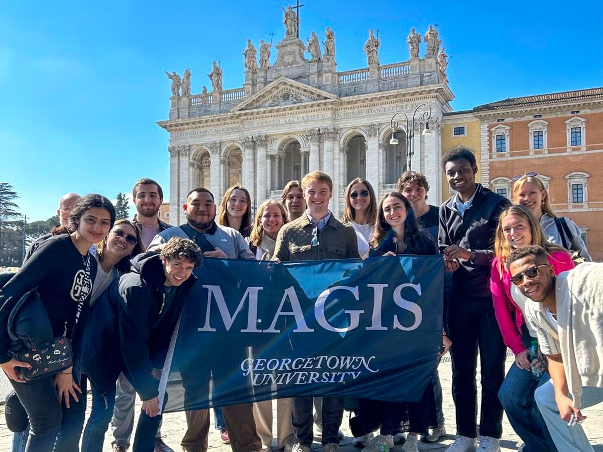 students posing in front of some kind of fancy building posing with the Magis Georgetown flag