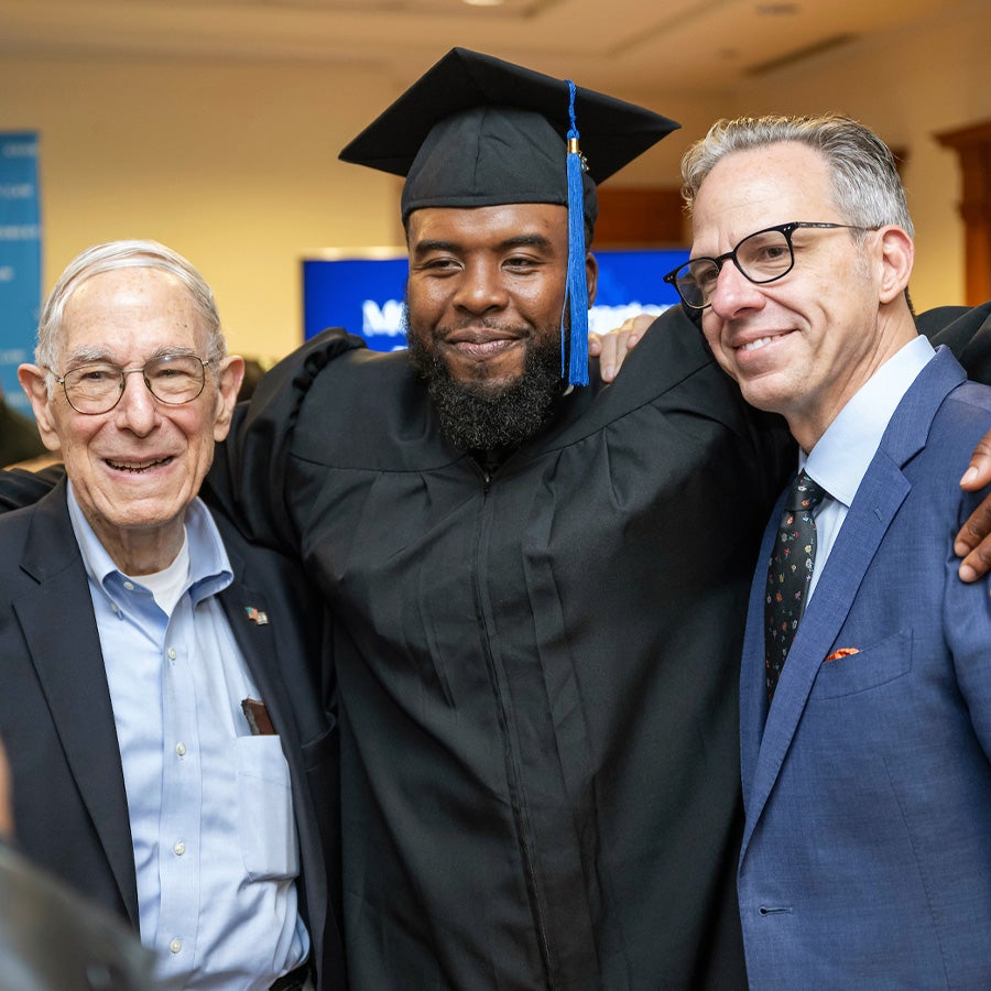 student at graduation posing with professors